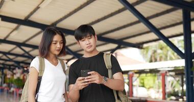 retrato de feliz casal asiático verifica a localização no mapa on-line do smartphone na estação de trem. sorrindo masculino e feminino usando o aplicativo de mapa de navegação do telefone móvel. conceito de férias, viagens e hobby. video