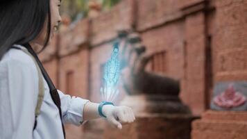 portret zijaanzicht van aziatische vrouw die op een slimme horloge drukt terwijl ze in de oude tempel staat. zichtbaar ar-scherm projecteren en chatten tijdens een videogesprek. futuristisch en technologisch concept video