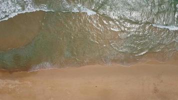 vista aérea de la playa de arena blanca y la textura de la superficie del agua. olas espumosas con cielo. hermosa playa tropical. increíble costa de arena con olas de mar blanco. concepto de naturaleza, paisaje marino y verano. video
