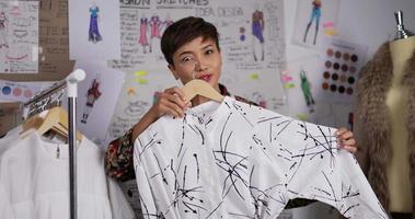 retrato de diseñador de moda o estilista asiático transmitiendo en vivo en las redes sociales sobre la nueva colección de ropa en el estudio. sastre mujer modistas prepara ropa de armario para la venta. video