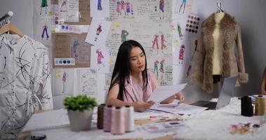 mulher professora asiática ajudando uma estudante de moda olhando um esboço de roupas femininas no estúdio. designer de moda, conceito de treinamento e educação. video