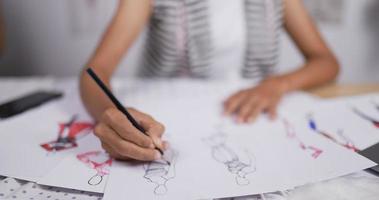 Close up hand of Fashion designer woman draws a sketch of women's clothing while sitting at the studio. Happy startup small businesswoman is in process of creating a new clothes collection. video