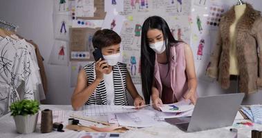 retrato de duas mulheres asiáticas de estilista olhando um esboço de roupas femininas no laptop e falando ao telefone com o cliente no estúdio. conceito de negócio sme. video