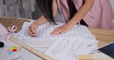 Close up of Professional Asian fashion designer measuring fabric according to the pattern in a modern studio. Young woman creating new clothing collections at work. video