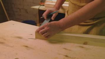 A mature man makes a marking on a board that he has sanded with a grinding machine