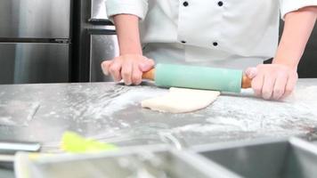 Close up of chef's hand in white cook uniforms with aprons are kneading pastry dough with roller, preparing bread, pies, and fresh bakery food, baking in oven at stainless steel kitchen of restaurant. video