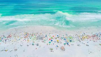 Aerial locked shot of waves breaking on the shore. Colourful beach umbrellas and people enjoying the summer. photo