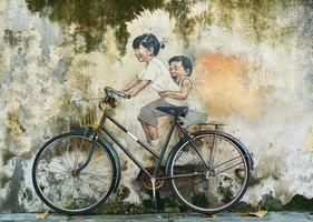 niños pequeños en un mural de arte callejero en bicicleta en george town, penang, malasia. foto