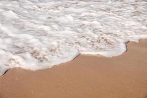 Soft waves with foam of ocean on the sandy beach background photo