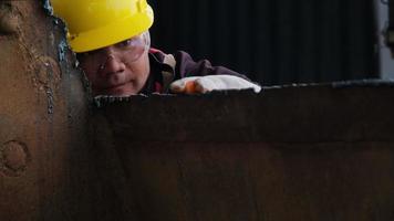 un travailleur masculin portant des lunettes et des gants de construction inspecte le travail après avoir meulé du métal avec une meuleuse d'angle dans un atelier à domicile. video