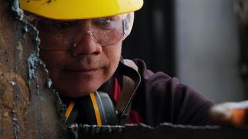 un travailleur masculin portant des lunettes et des gants de construction inspecte le travail après avoir meulé du métal avec une meuleuse d'angle dans un atelier à domicile. video