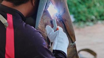 Skilled metalworkers wearing welding masks and gloves work in the home workshop with an arc welding machine. Worker welding metal with sparks, close-up video