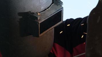 Skilled metalworkers wearing welding masks and gloves work in the home workshop with an arc welding machine. Worker welding metal with sparks, close-up video