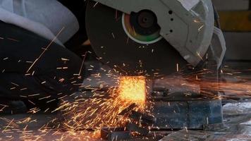 Professional men wearing goggles and construction gloves work in home workshop with electric steel cutter machine. Cutting metal makes sparks flying, closeup video