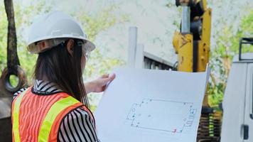 la ingeniera mira los planos del proyecto e inspecciona el trabajo mientras está de pie en un sitio de construcción. video