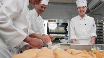 A group of professional gourmet team, four chefs in white cook uniforms and aprons knead pastry dough and eggs, prepare bread, and bakery food, baking in an oven at stainless steel restaurant kitchen. video