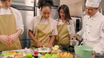 curso de cocina de hobby, chef masculino senior en uniforme de cocinero enseña a los jóvenes estudiantes de cocina a pelar y picar manzanas, ingredientes para pasteles, pasteles de frutas en la cocina de acero inoxidable del restaurante. video