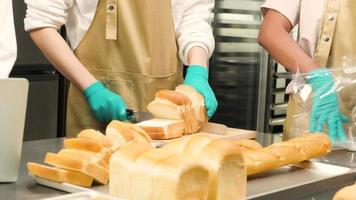 close-up das mãos do chef cortando e dividindo o pão fresco na placa de madeira com faca para embalagem e entrega na cozinha culinária. produto caseiro saudável para uma saborosa refeição de café da manhã.