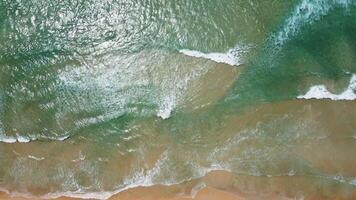 vista aérea de la playa de arena blanca y la textura de la superficie del agua. olas espumosas con cielo. hermosa playa tropical. increíble costa de arena con olas de mar blanco. concepto de naturaleza, paisaje marino y verano. video