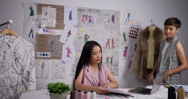 asiatische lehrerin hilft einem modestudentenmädchen, das im studio eine skizze von damenbekleidung sucht. modedesigner, ausbildungs- und bildungskonzept.