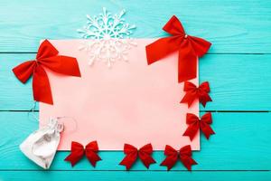 Frame of red bows with winter accessories on blue wooden background. Top view photo