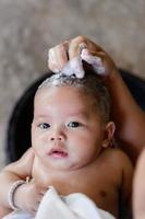 Happy smiling baby newborn taking a bath and looking at camera with beautiful brown eyes. Mother of little child in mom arms cleaning and bathing infant head with cute smile face boy at home photo