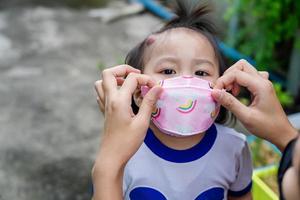 Adorable little child girl with big capillary strawberry hemangiomas red birthmark on head refuses to wear medical face mask that the mother or guardian are trying to put on face. Health care concept photo