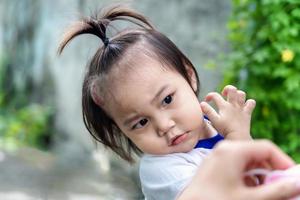 Adorable little child girl with big capillary strawberry hemangiomas red birthmark on head refuses to wear medical face mask that the mother or guardian are trying to put on face. Health care concept photo