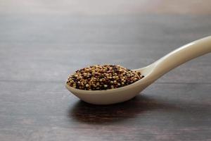 Quinoa seeds in the white spoon isolated on wooden table background.  Quinoa is a good source of protein for people following a plant-based diet. photo