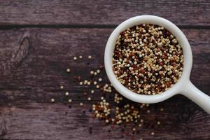 Quinoa seeds in the white cup on wooden background.  Quinoa is a good source of protein for people following a plant-based diet. photo