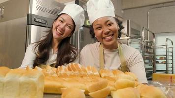 Porträt von professionellen Köchinnen in Uniform, die mit fröhlichem Lächeln in die Kamera blicken und stolz auf ein Tablett mit Brot in der Küche sind. ein Freund und Partner von Backwaren und täglich frischer Bäckerbeschäftigung. video