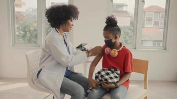 African american doctor is applying plaster to a child's shoulder after being vaccinated. Opening sleeves to vaccinate against flu or epidemic in health care and vaccinated concept.