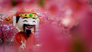 Chinese god of prosperity mascot with blurry fake blossom flower video