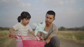 4k Video slow-motion, A father is teaching his daughter to learn to play with a turbine in the grass. Happily in the evening. Family concept.