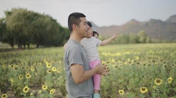 un padre asiático llevó felizmente a su hija al campo de girasoles. durante la puesta de sol