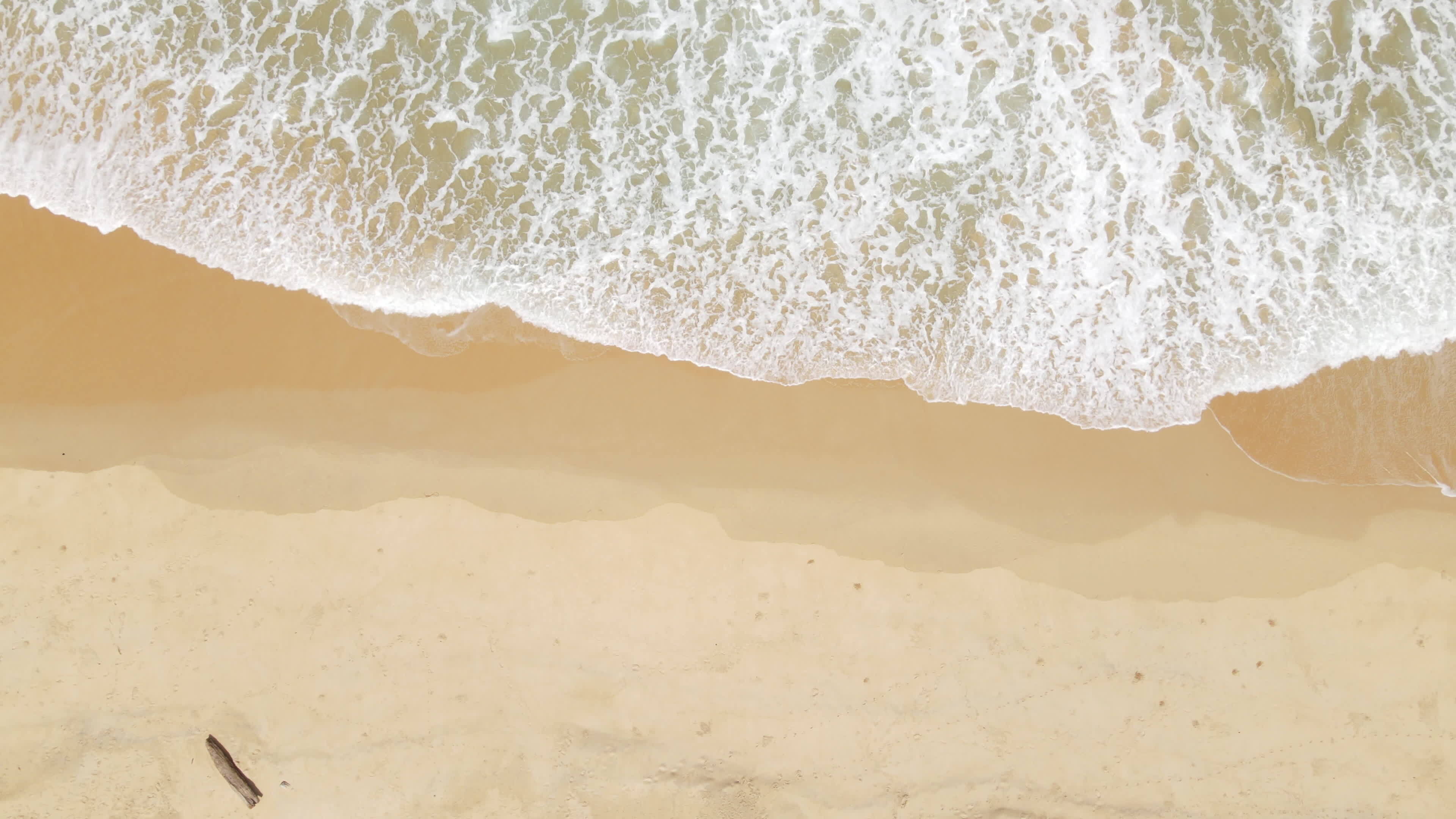 Zoom in aerial view of sand beach and water surface texture. Foamy