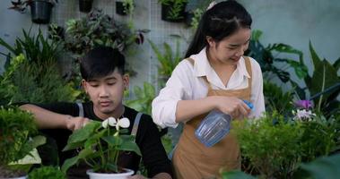 portret van een gelukkig jong Aziatisch paar dat samen in de tuin tuiniert en naar de camera kijkt. vrouwelijke tuinman met een spuitfles water geven op bladplanten en mannelijke tuinman met lepel op de plant.