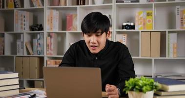 retrato de empresário asiático surpreso recebe boas notícias depois de olhar para um laptop. homem empreendedor de sucesso usando notebook de computador no escritório em casa. distanciamento social e trabalho em casa conceito. video