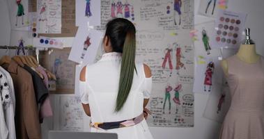 vue arrière d'une créatrice de mode professionnelle contemplant des dessins en studio. femme d'affaires asiatique heureuse regardant le conseil d'administration et pensant. concept de concepteur et de propriétaire d'entreprise.