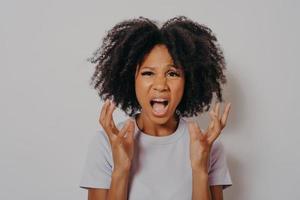 Young beautiful African American woman with curly hair standing angry and mad, raising hands up photo