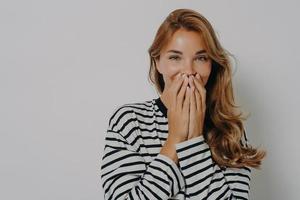 Beautiful cheerful woman giggles positively covers mouth with hands tries to hide emotions
