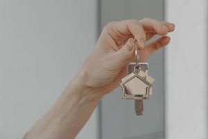 Woman holding house shaped keychain, selective focuse on female hand with key from new home photo