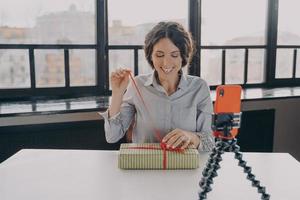 Excited hispanic woman blogger opening gift box recording video about xmas present for her blog photo