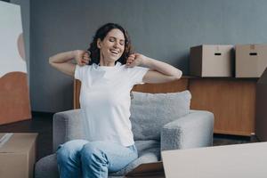Happy young woman moves alone. Girl is stretching and going to load packed box. photo