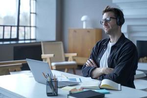 Positive German man bank employee sitting at workplace at modern home office in wireless headphones photo