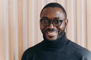 Elegant confident Afro american businessman in glasses posing while standing in modern office photo