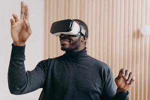 Smiling african american businessman in VR glasses sits in office, testing virtual reality goggles photo