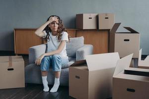 Headache from moving. Exhausted spanish woman sitting among packed cardboard boxes. photo