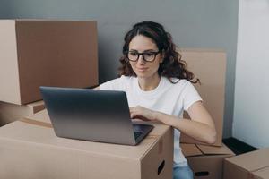 Girl in white t-shirt and glasses is texting on computer ordering delivery service for packed boxes. photo