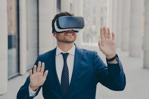 Young excited man in suit standing on city street and testing VR glasses or 3d goggles photo